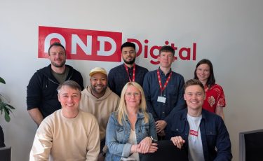 8 people standing in front of a sign that reads 'AND Digital'